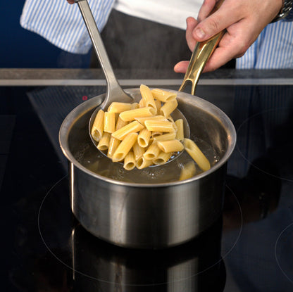 Pasta being served from a titanium pot with a ladle on a stove.