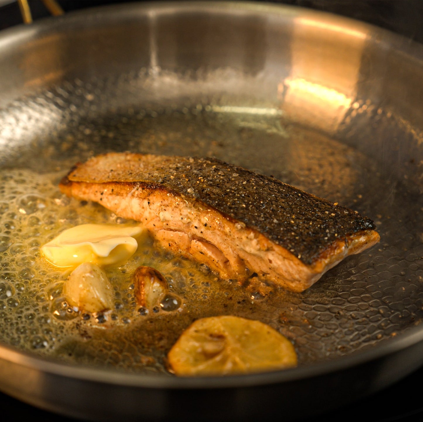Salmon fillet cooking in a titanium pan with lemon slices.